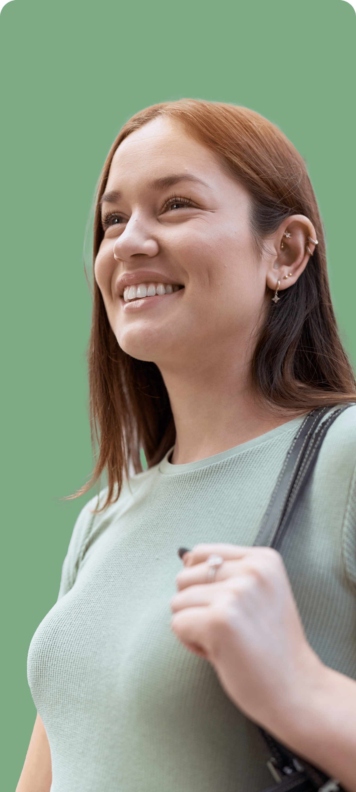 Smiling young woman with reddish-brown hair wearing a light green top, holding a bag, representing confidence and emotional well-being in mental health context.